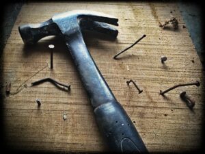 Skills for coding by showing a hammer and various nails not fixed correctly on a wooden board.